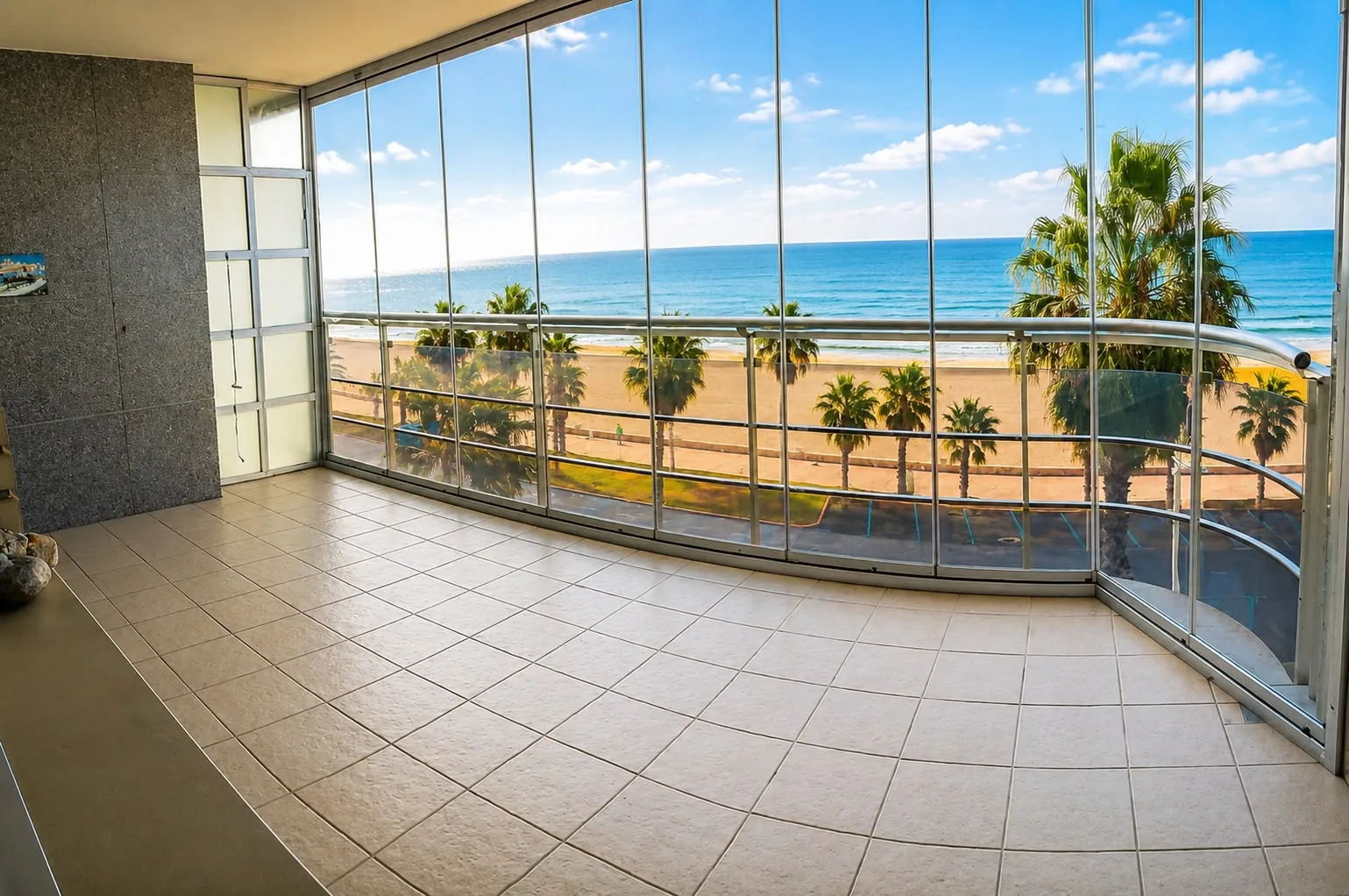 Terrasse vitrée avec vue panoramique sur la plage, la promenade et les palmiers